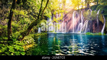 Letztes Sonnenlicht erhellt den reinen Wasserfall im Plitvice National Park. Buntes Frühlingspanorama von grünem Wald mit blauem See. Tolle Landschaft Stockfoto