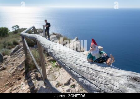 Keramik-Gnom auf einem Zaun am Aussichtspunkt Cerro Gordo mit dem Meer und einem Mann im Hintergrund Stockfoto