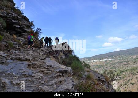 Wanderer, die die Scarihuela de Fondales erklimmen, ein enger Pfad, der den Berg hinaufwindet. Pfad entlang einer Klippe. La Taha in der Alpujarra Stockfoto