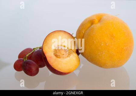 Halbpflaumengelber Pfirsich und rote Trauben im mediterranen Sonnenlicht süße Früchte aus nächster Nähe Stockfoto
