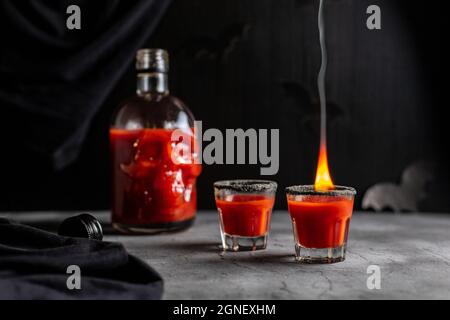 Tomatencocktail in einer kopfförmigen Flasche und Gläser mit Feuer. Getränk für Halloween-Party auf dunklem Hintergrund Stockfoto