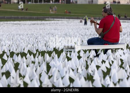 Genf, USA. September 2021. Ein Mann sitzt neben weißen Fahnen, die auf der National Mall angebracht sind, um das Leben zu ehren, das COVID-19 in Washington, DC, USA, am 18. September 2021, verloren gegangen ist. Kredit: Aaron Schwartz/Xinhua/Alamy Live Nachrichten Stockfoto
