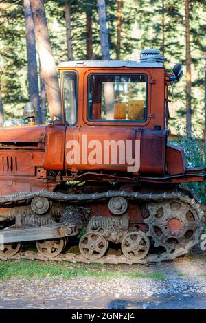 Ein alter rostiger Traktor steht in der Nähe der Scheune. Auf dem grünen Gras steht ein roter alter Traktor für den Haushalt und die Ernte. Stockfoto