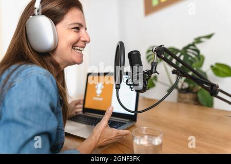 Reife Frau, die aus ihrem Heimstudio einen Podcast mit Mikrofon und Laptop aufnahm Stockfoto