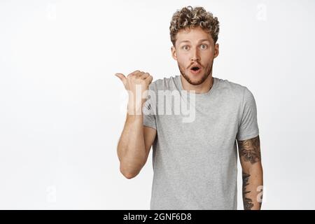 Enthusiastischer junger Mann, der mit dem Finger nach links zeigt, begeistert und begeistert vom Verkaufsangebot, mit Preis oder Logo, weißem Hintergrund Stockfoto