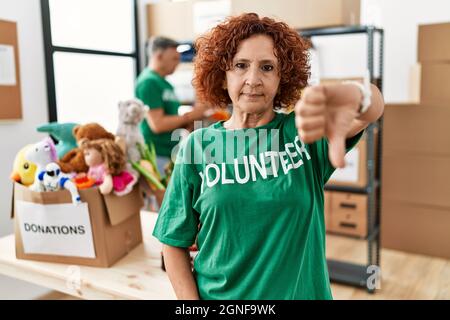 Frau mittleren Alters trägt Freiwilligen T-Shirt bei Spenden stehen unglücklich und wütend, Ablehnung und negativ mit Daumen nach unten Geste. Schlecht e Stockfoto