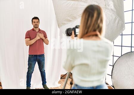 Fotografin spricht Bilder von einem Mann, der als Model im Fotostudio posiert und lächelt mit Händen auf der Brust, geschlossenen Augen und dankbarer Geste Stockfoto