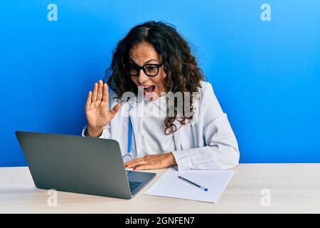 Schöne Arzt mittleren Alters Frau tut Videoanruf winken auf Laptop feiern verrückt und erstaunt für den Erfolg mit offenen Augen schreiend aufgeregt. Stockfoto