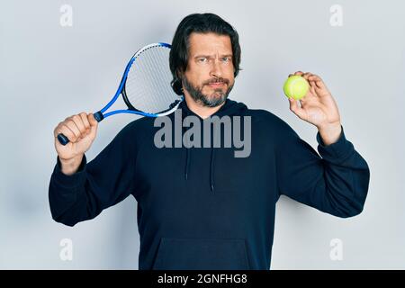 Kaukasischer Mann mittleren Alters spielt Tennis mit Schläger und Ball skeptisch und nervös, runzelte die Stirn wegen des Problems. Negative Person. Stockfoto