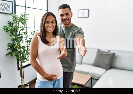 Junge interracial Paar erwartet ein Baby, berühren schwangeren Bauch lächelnd freundlich bietet Handschlag als Gruß und einladend. Erfolgreiches Geschäft. Stockfoto