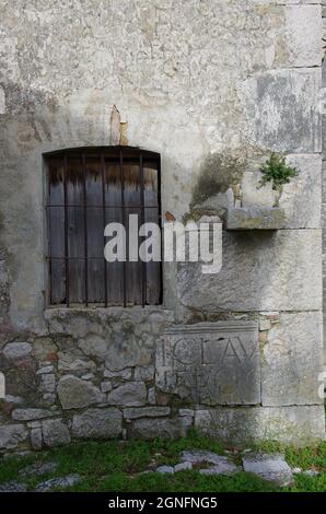 Archäologische Stätte von Altilia, Molise, Italien: Ein altes Fenster mit Gitter und einer unbekannten Inschrift erscheint auf den Resten einer alten Mauer. Stockfoto