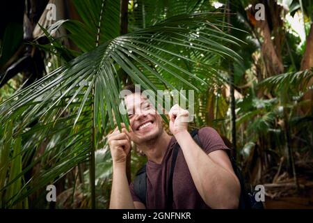 Glücklicher Mann entdeckt Dschungel. Lustiges Porträt von Reisenden im tropischen Regenwald auf den Seychellen. Stockfoto
