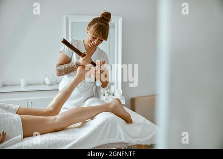 Conident weibliche Spezialist tut Bein-Massage mit Bambus-Stick, um schöne kaukasische Frau Client Stockfoto