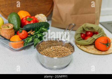 Gesundes Frühstückscerealien. Verschiedene rohe Cerealien, Gemüse, Kräuter auf dem Küchentisch. Frisches rohes Frühstück Müsli Essen in der eigenen Küche. Vegetarisch Stockfoto