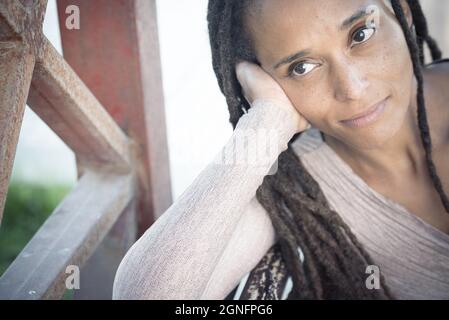 Nahaufnahme einer afroamerikanischen Frau mit einer langen geflochtenen Frisur, die ihr Gesicht auf ihrer Handfläche ruht und nach draußen schaut. Nachdenkliche Frau mit Zopf Stockfoto