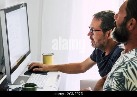 Zwei Mitarbeiter arbeiten zusammen am Desktop-Computer. Reife Männer arbeiten als Team, während sie Desktop-Computer verwenden. Zwei Männer arbeiten am Computer, readi Stockfoto