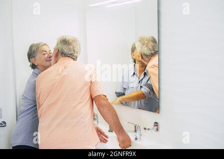 Romantisches Seniorenpaar, das zu Hause im Badezimmer die Hände wäscht. Ein älteres Paar im Bad. Liebevolles altes Paar, das sich vor einander küsst Stockfoto