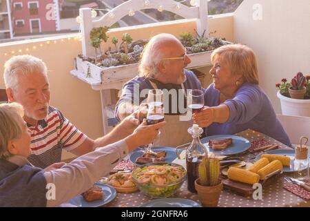 Fröhliche zwei ältere Paare feiern zusammen mit einem Glas Wein auf der Terrasse Party. Ältere Menschen haben Spaß beim Essen auf dem Dach. Alte Peopl Stockfoto