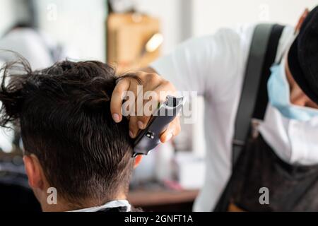 Friseur mit Gesichtsmaske mit Haarschneider auf Client. Stylisten schneiden Haare Stockfoto