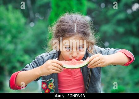 Kleines niedliches Mädchen, das im Garten eine saftige Wassermelone isst. Kinder essen Obst im Freien. Gesunde Ernährung für Kinder. Stockfoto