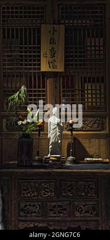 Weißer Buddha-Statuette-Hausaltar mit Blumen-Pflanzen-zwei Kerzen. Shuyuanmen Kalligraphie Straße-Xi'an-China-1576 Stockfoto