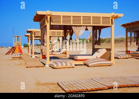 Holzpavillon am Strand mit Sonnenliegen und Vorhängen, leere Vordächer am Strand. Stockfoto