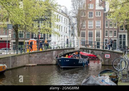 Amsterdam, Niederlande - April 2019: Touristenboot, das unter einer schmalen Brücke in einem der vielen Kanäle Amsterdams fährt Stockfoto