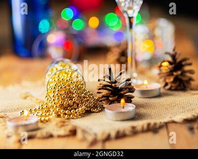 Zwei Sektgläser mit Weihnachtsperlen. Weihnachtsdekorationen im rustikalen Stil auf hellem Hintergrund mit Lichtern. Kiefernzapfen und brennende Kerzen an Stockfoto