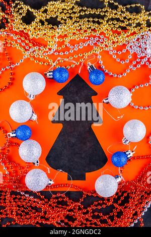 Weihnachtsperlen auf dunklem Hintergrund. Weihnachtskugeln, bunte Perlen und Weihnachtsbaum. Papiergeschnittener weihnachtsbaum. Draufsicht Stockfoto