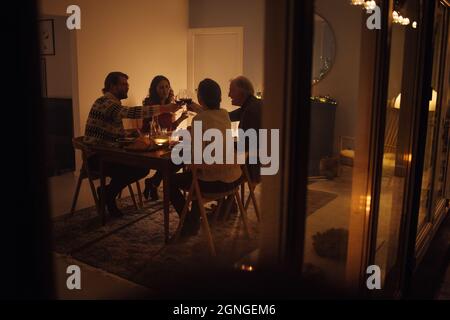 Familie, die am Heiligabend am Esstisch Wein toasting. Familie, die ein gemeinsames Weihnachtsessen in einem gemütlichen skandinavischen Zuhause hat. Stockfoto