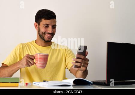 Junger Student macht einen Videoanruf mit einem Lächeln auf seinem Gesicht. Geschäftsmann macht eine Videokonferenz mit einer Tasse Kaffee Stockfoto