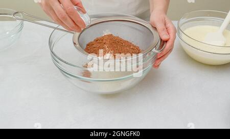 Schokoladenkuchen Schritt für Schritt Rezept. Mischen von trockenen Zutaten - Mehl, Kakaopulver, Backpulver - in einer Glasschüssel, Nahaufnahme Stockfoto