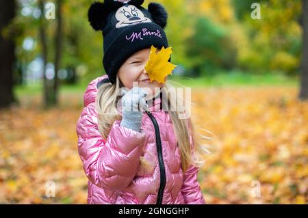 Ein Mädchen hält ein großes, gelbes Ahornblatt in ihren Händen. Stockfoto