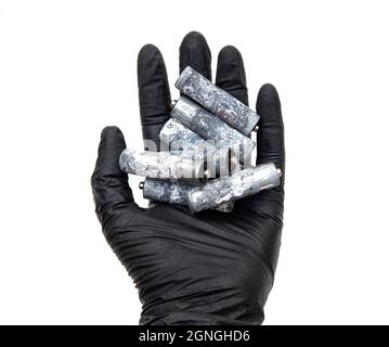 Nahaufnahme einer menschlichen Hand in schwarzem Nitril-Handschuh mit einer Reihe stark korrodierter AA-Batterien auf weißem Hintergrund. Stockfoto