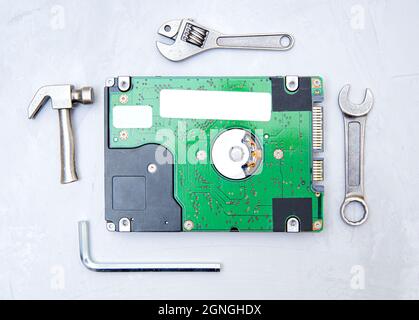 Festplatte ohne Abdeckung, eingerahmt von kleinen Kopien beliebter Handwerkzeuge auf einem konkreten Hintergrund. Das Konzept der Verwendung geeigneter Werkzeuge für die Arbeit. Stockfoto
