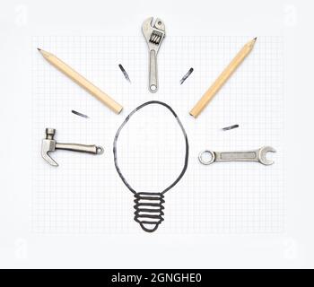 Handwerkzeuge und Graphitstifte, die die Strahlen einer Glühbirne auf einem Blatt Papier mit quadratischer Rulierung zeichnen. Konzept zur Ideenentwicklung. Stockfoto