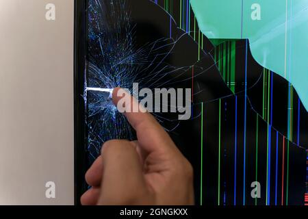 Der lcd-Monitor ist kaputt, die Hand eines Mannes berührt einen Riss. Stockfoto