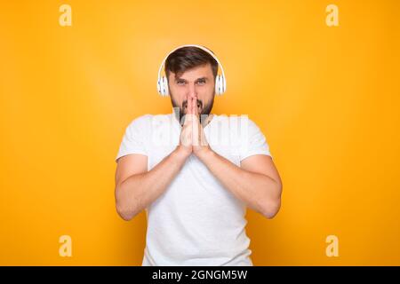 Ein Mann, der mit weißen Kopfhörern Musik hörte, faltete seine Handflächen vor seinem Gesicht. Stockfoto