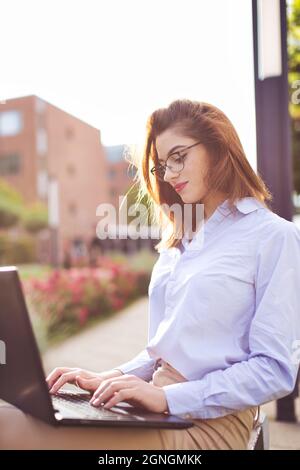 Junge freiberufliche kaukasische Programmiererin Frau, die im Park an einem Laptop arbeitet Stockfoto