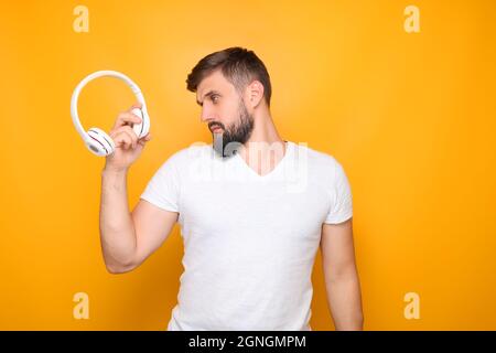 Bärtiger Mann, Musikliebhaber hält weiße Kopfhörer vor sich. Stockfoto