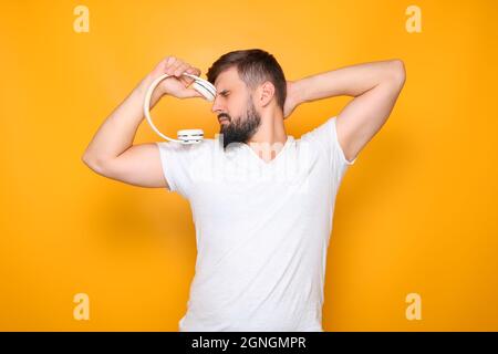 Ein Mann hält weiße Kopfhörer in der Hand und schließt die Augen. Stockfoto