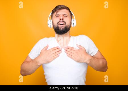 Bärtiger Mann in weißen Kopfhörern, der energische Musik hört und emotional singt. Stockfoto