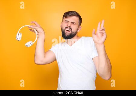 Ein Mann - Musikliebhaber in einem weißen T-Shirt, hält weiße musikalische Kopfhörer in seinen Händen. Stockfoto