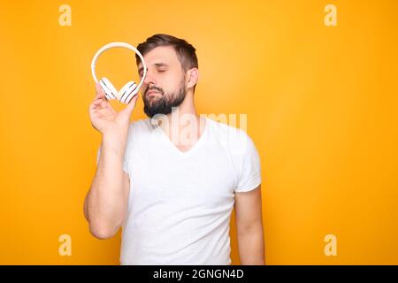 Ein Mann - Musikliebhaber in einem weißen T-Shirt, hält weiße musikalische Kopfhörer in seinen Händen. Stockfoto
