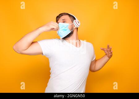 Ein Mann, der eine medizinische Maske auf seinem Gesicht und musikalische Kopfhörer trägt, zeigt verschiedene Gesten. Stockfoto