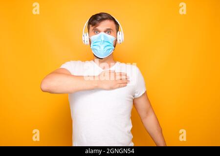 Ein Mann, der eine medizinische Maske auf seinem Gesicht und musikalische Kopfhörer trägt, zeigt verschiedene Gesten. Stockfoto