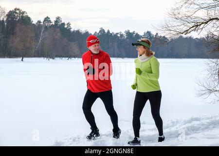 Lächelndes Seniorenpaar joggt im verschneiten Winterpark. Stockfoto
