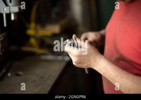 Ein Mann zieht einen Bohrer heraus. Installieren einer Bohrmaschine für eine Bohrmaschine. Arbeitet in der Garage. Die Hände des Meisters halten den Teil der elektrischen Ausrüstung für das Drillin fest Stockfoto