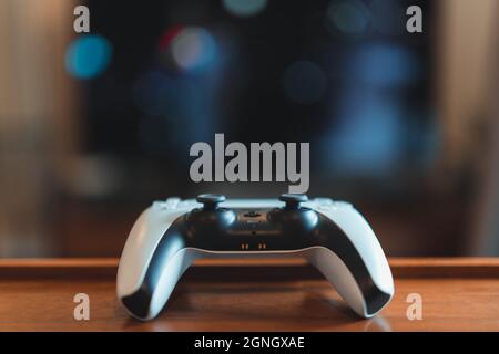 London, Großbritannien – 25. Mai 2021: Ein weißer PlayStation 5 (PS5)-Controller auf dem Tisch, tv im Hintergrund, selektiver Fokus. PlayStation 5 ist das neueste Video Stockfoto