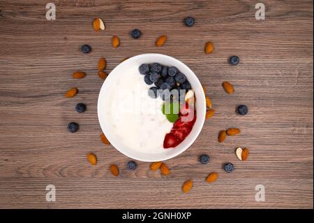 Schüssel Hafergranola Müsli mit Joghurt, frischen Erdbeeren, Heidelbeeren und Mandeln auf einem Holzbrett für ein gesundes Frühstück. Draufsicht. Stockfoto